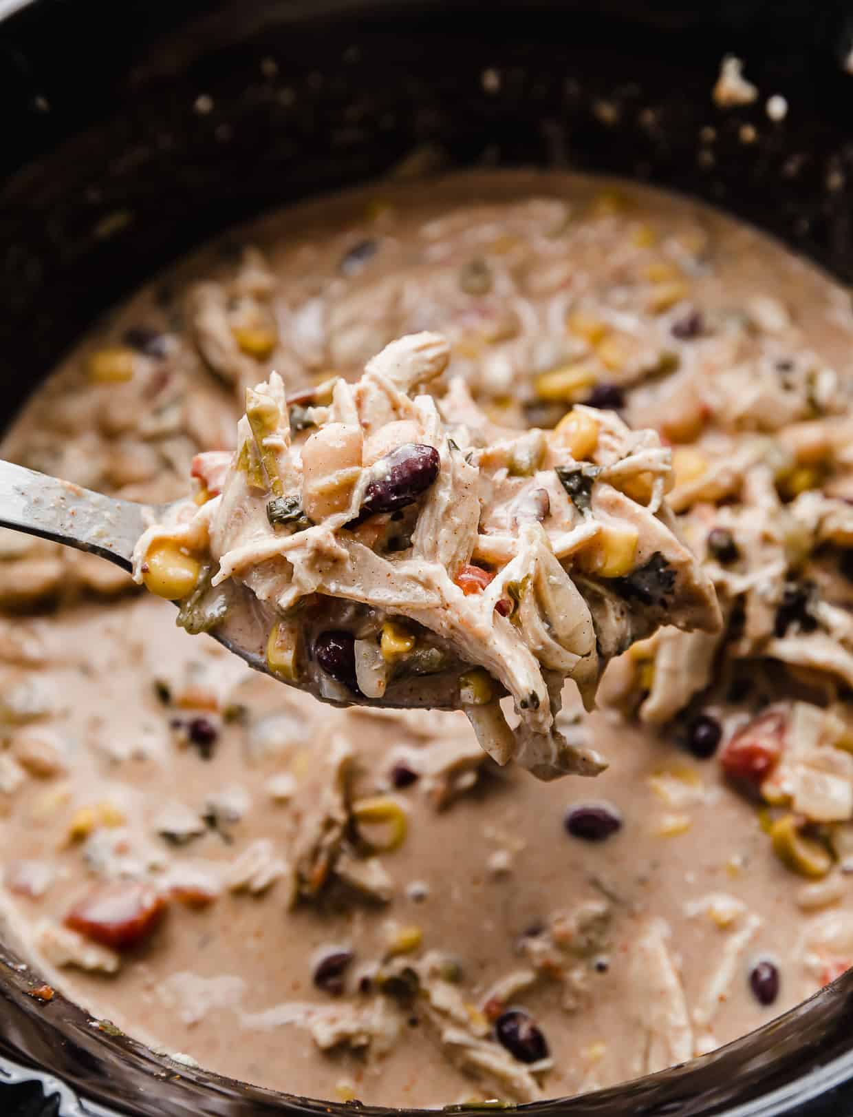 A metal spoon with cream cheese chicken chili with black beans and corn on the spoon.