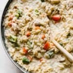 Cajun Chicken Orzo pasta in a skillet with a wooden spoon scooping the noodles.