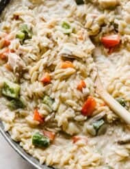Cajun Chicken Orzo pasta in a skillet with a wooden spoon scooping the noodles.