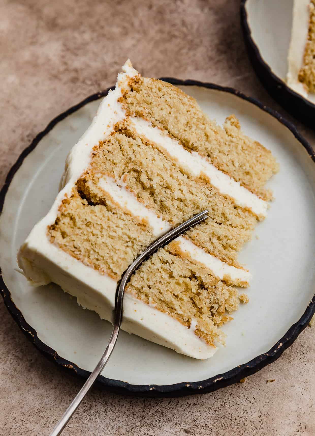 A slice of brown butter layer cake frosted with brown butter buttercream on a white plate.
