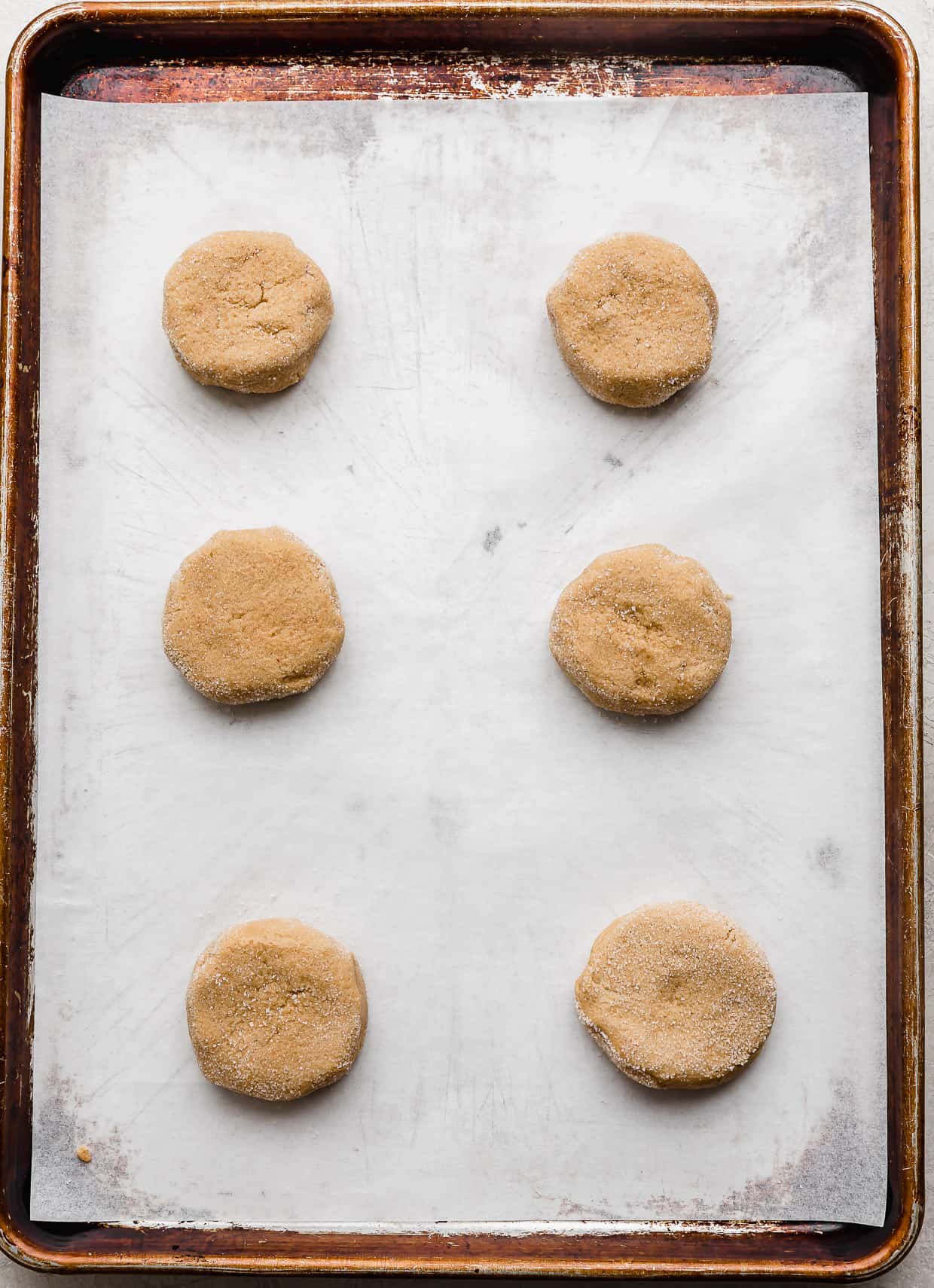 Six peanut butter cookie dough balls on a parchment lined baking sheet.