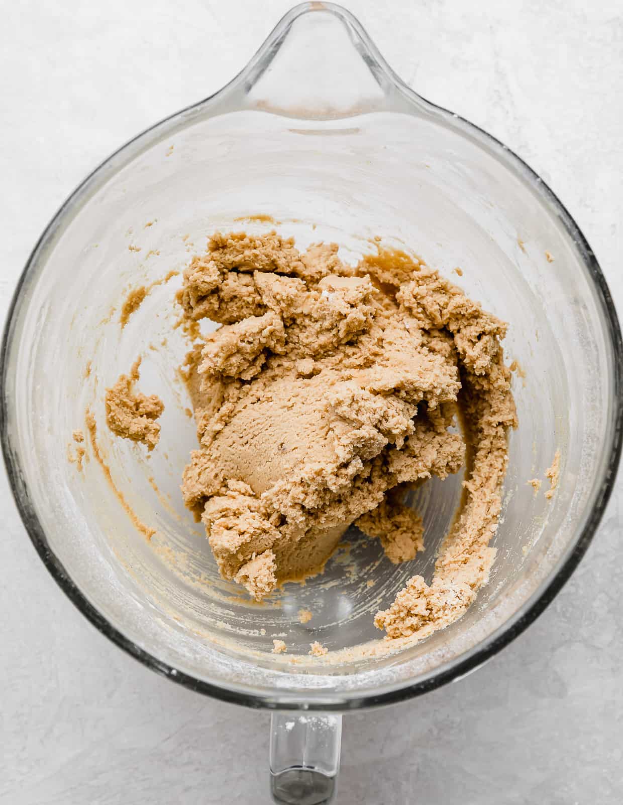 Crumbl Peanut Butter Blossom Cookie dough in a glass mixing bowl on a white background.