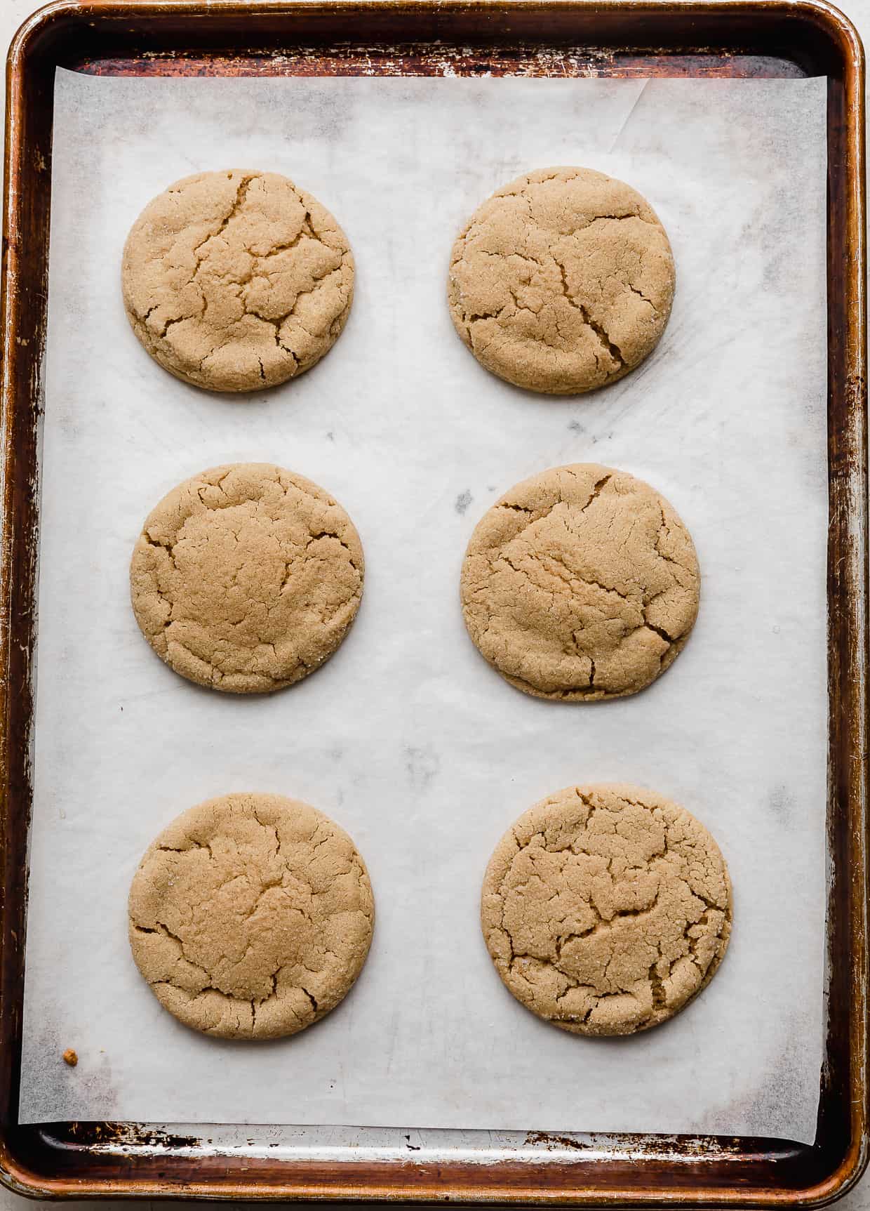 Six baked Crumbl Peanut Butter Blossom Cookies on a baking sheet.
