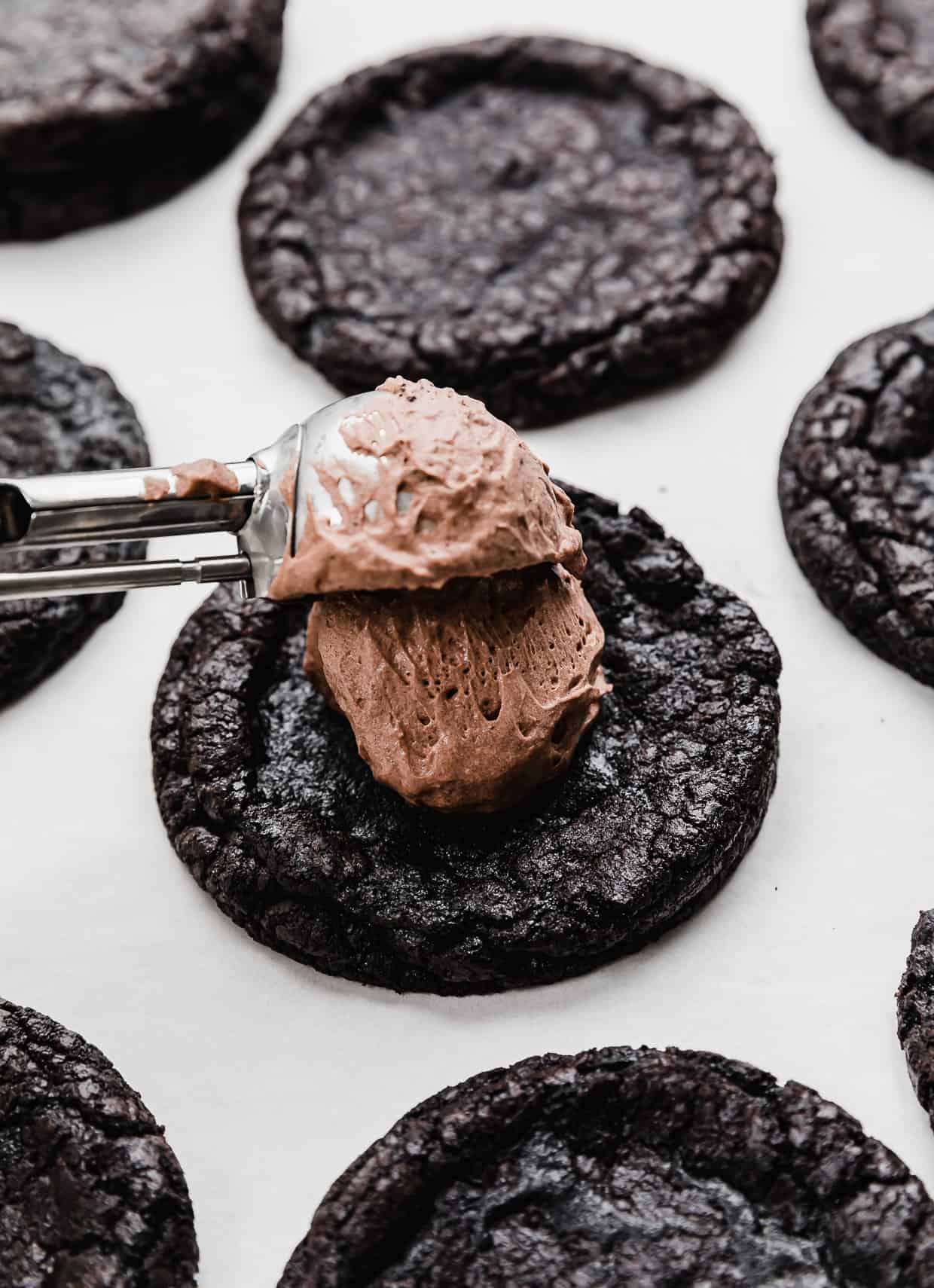 A cookie scoop putting chocolate mousse on top of a black cookie.