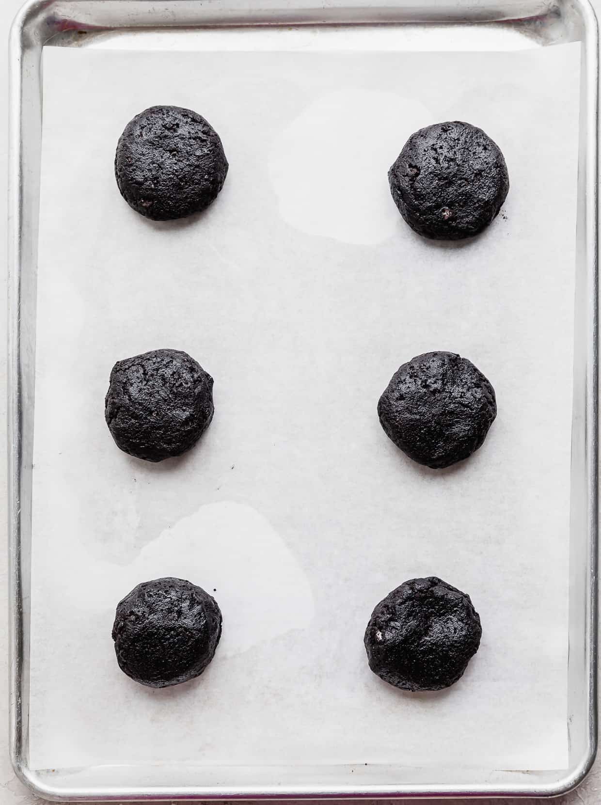 Six black Oreo cookie dough balls on a white parchment paper.
