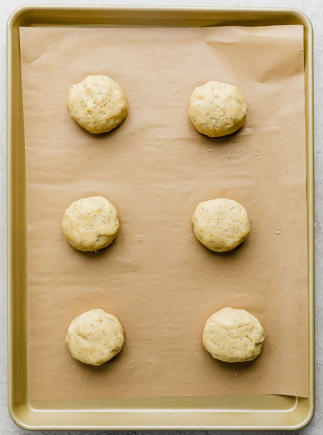 Lemon Poppy Seed Cookie dough balls on a tan parchment lined baking sheet, prior to baking.