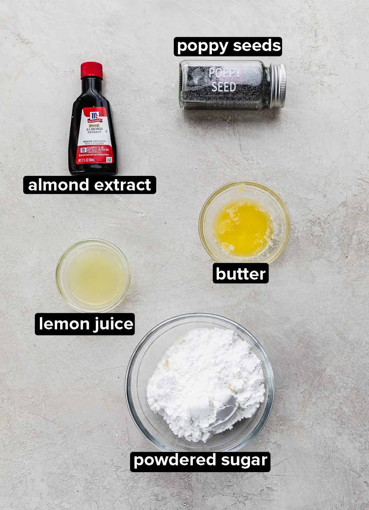 Almond extract, powdered sugar, lemon juice, butter, and poppy seeds on a gray background, used to make glaze for Lemon Poppy Seed Cookies.