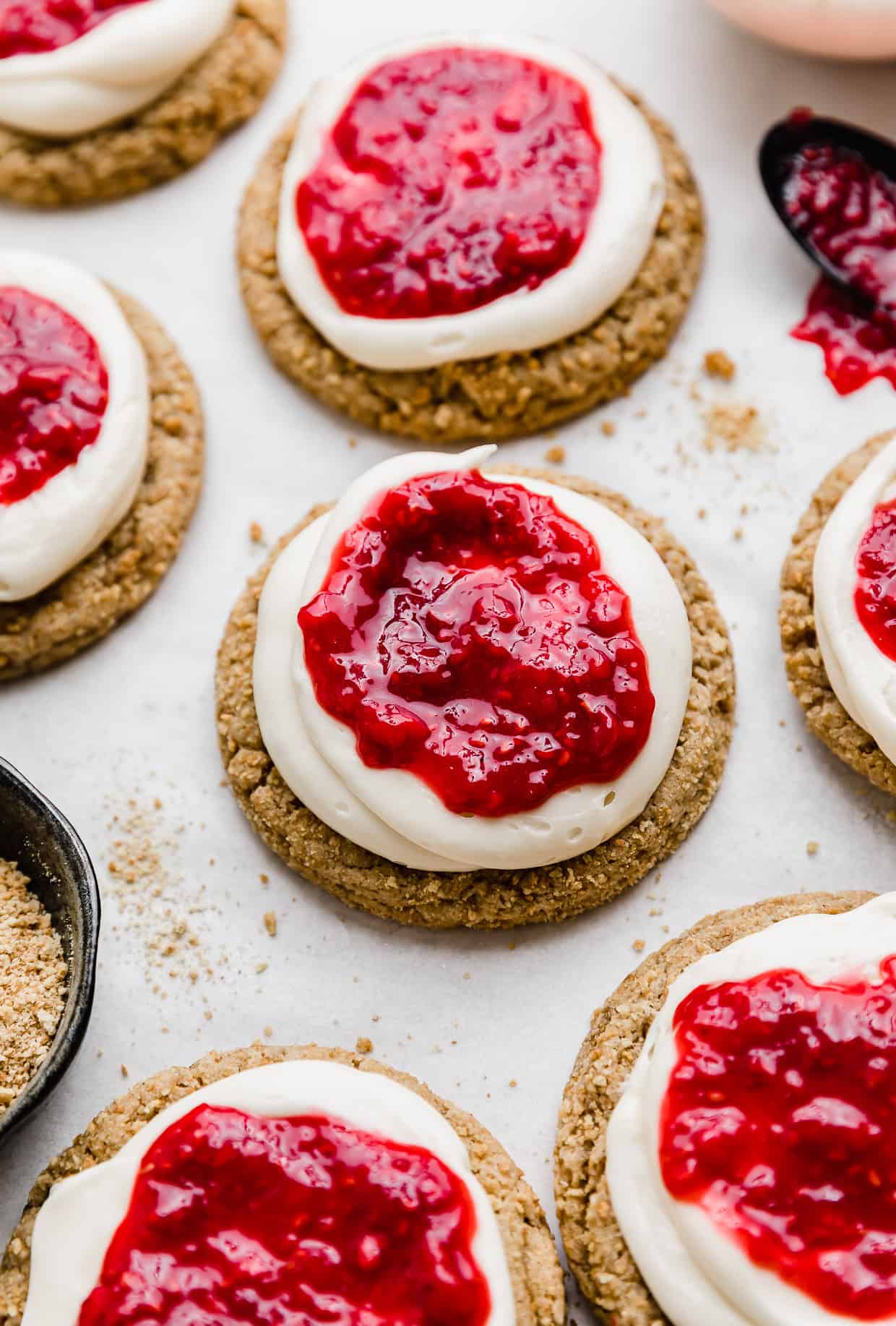 A Crumbl Raspberry Cheesecake Cookie made of a graham cracker cookie topped with a cream cheese frosting and raspberry sauce.