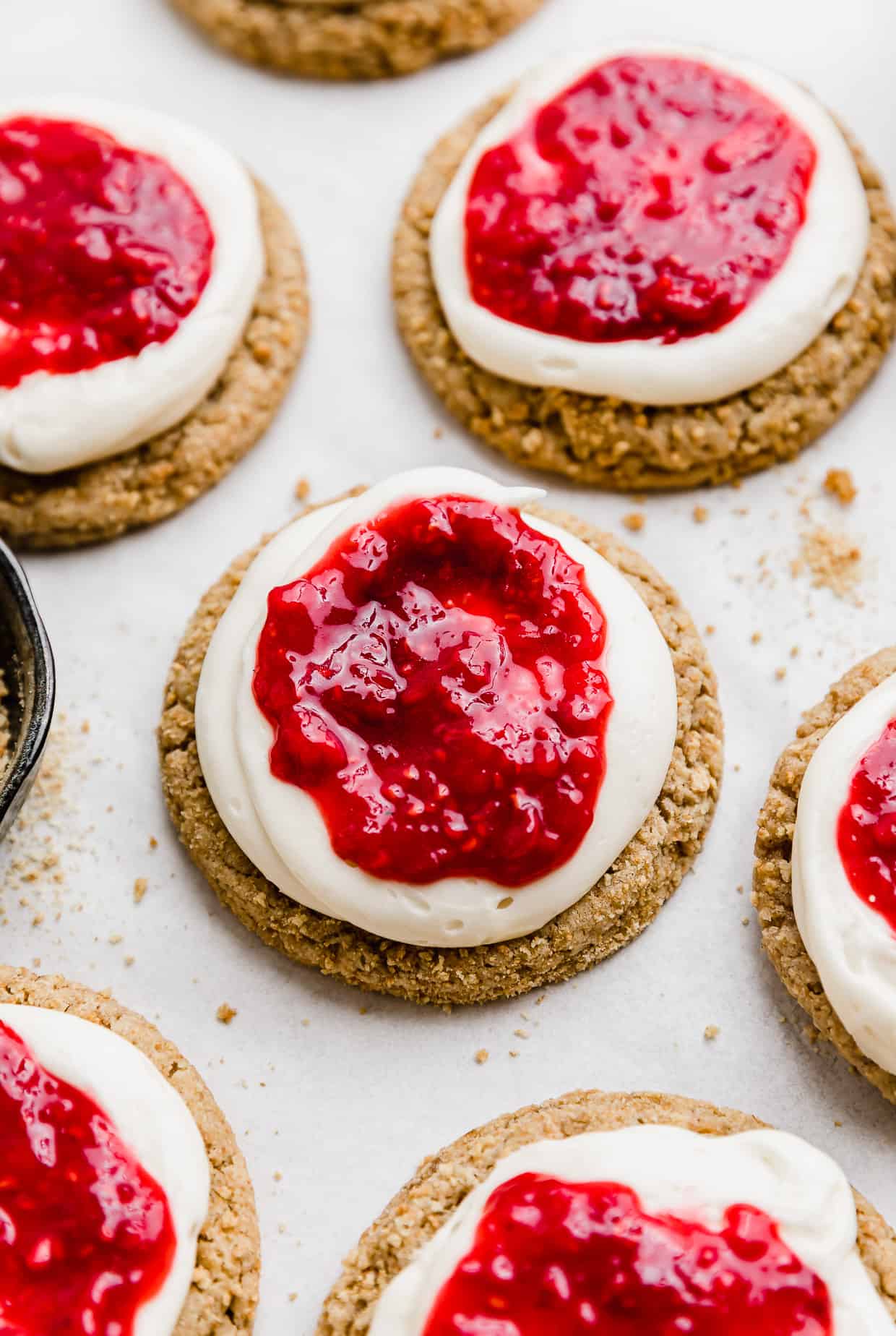A graham cracker cookie topped with cream cheese frosting and a raspberry sauce. 