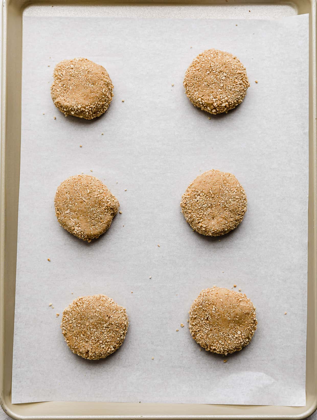 Six graham cracker cookie dough balls on a white parchment lined baking sheet.