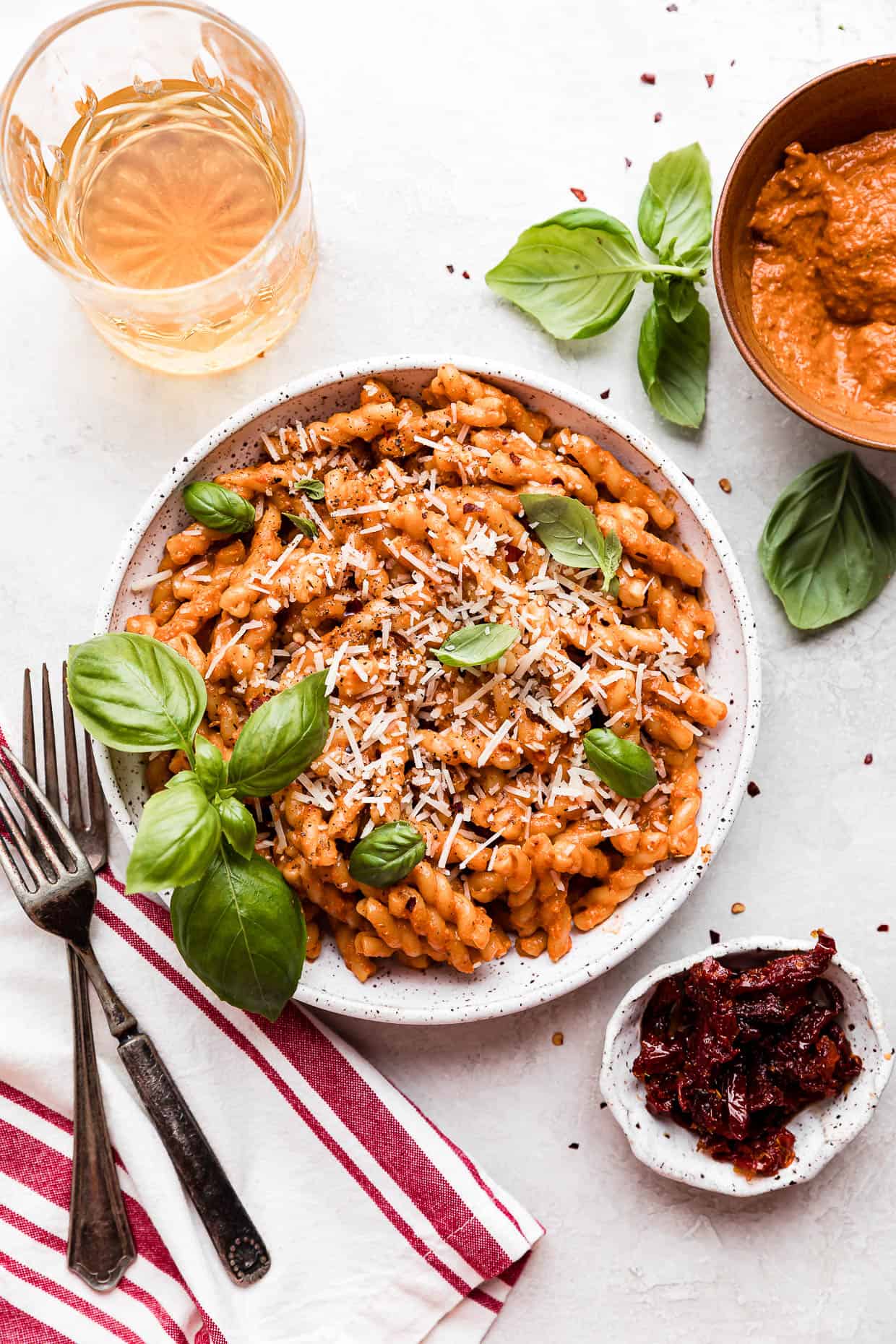 Red Pesto Pasta on a white plate topped with fresh basil, on a light gray background.