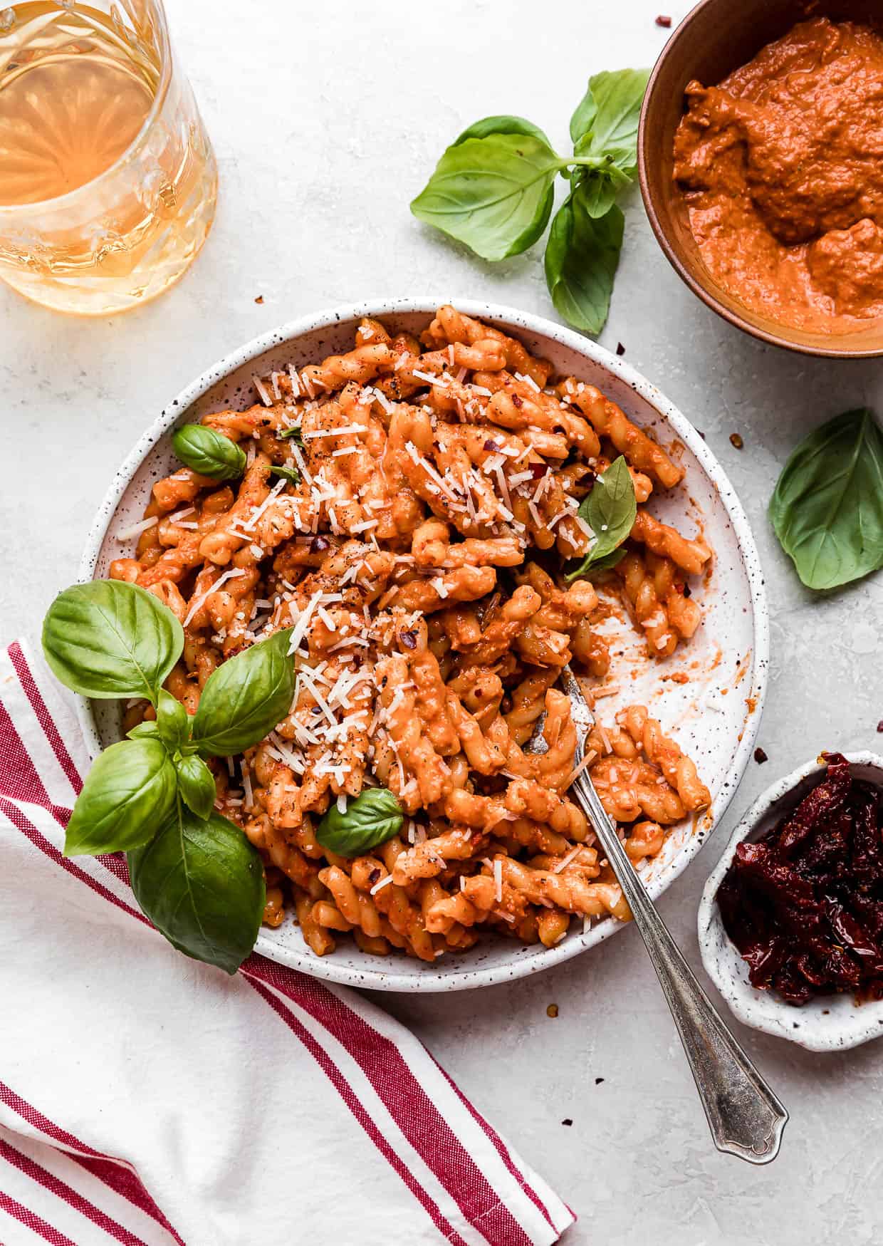 A fork in a bowl of Red Pesto Pasta topped with fresh basil.