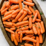 Roasted Baby Carrots topped with thyme and parsley on a bronze oval plate.