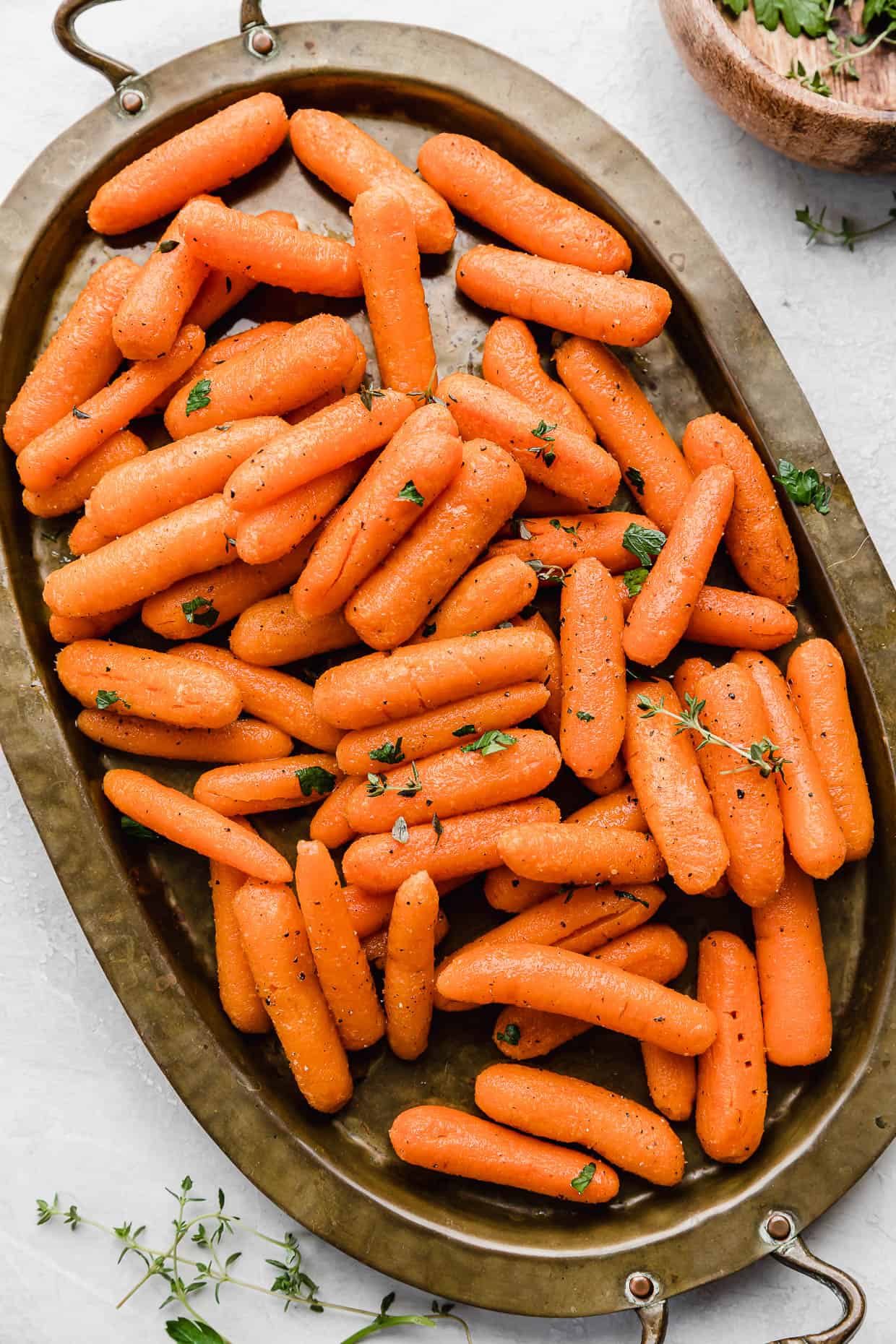 Roasted Baby Carrots topped with thyme and parsley on a bronze oval plate.