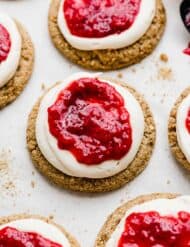 Raspberry Cheesecake Cookies: graham cracker cookie topped with cream cheese frosting, and raspberry sauce on a white background.