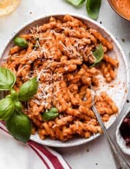 A white plate filled with Red Pesto Pasta topped with parmesan cheese and fresh basil.