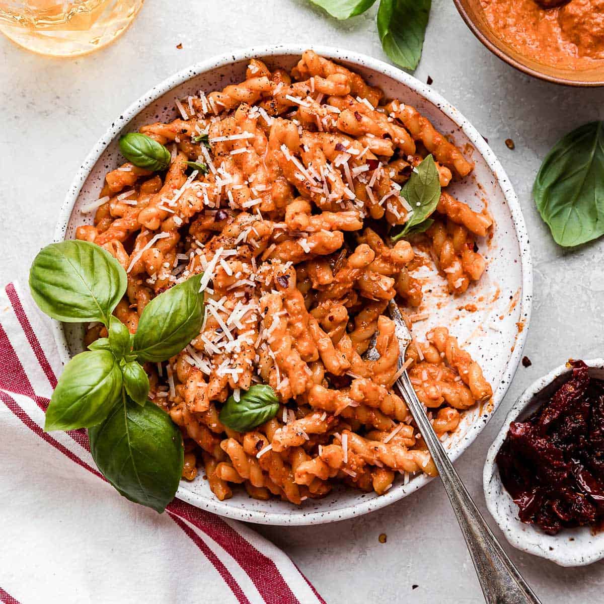 A white plate filled with Red Pesto Pasta topped with parmesan cheese and fresh basil.