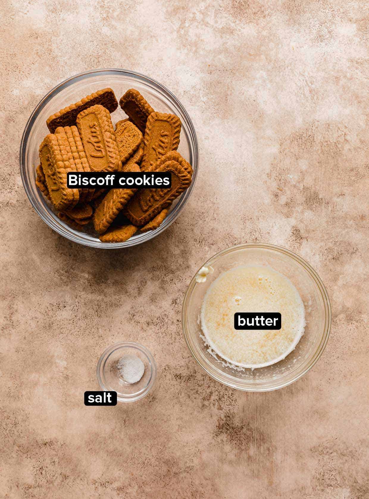Biscoff Pie Crust ingredients: biscoff cookies, melted butter, and salt, on a brown background.