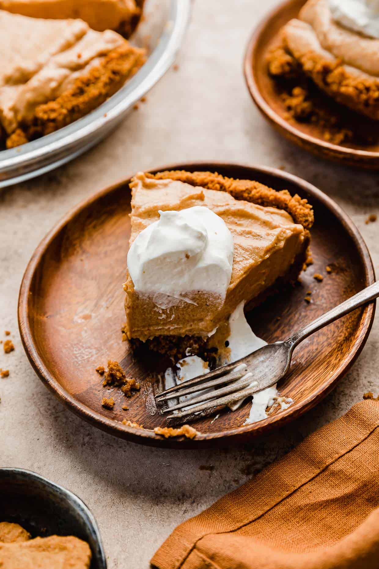 A slice of Biscoff Pumpkin Pie topped with whipped cream on a brown wood plate.