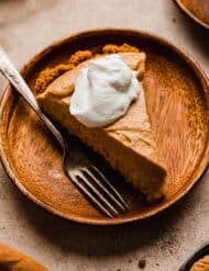 Biscoff Pumpkin Pie topped with whipped cream on a wood plate.