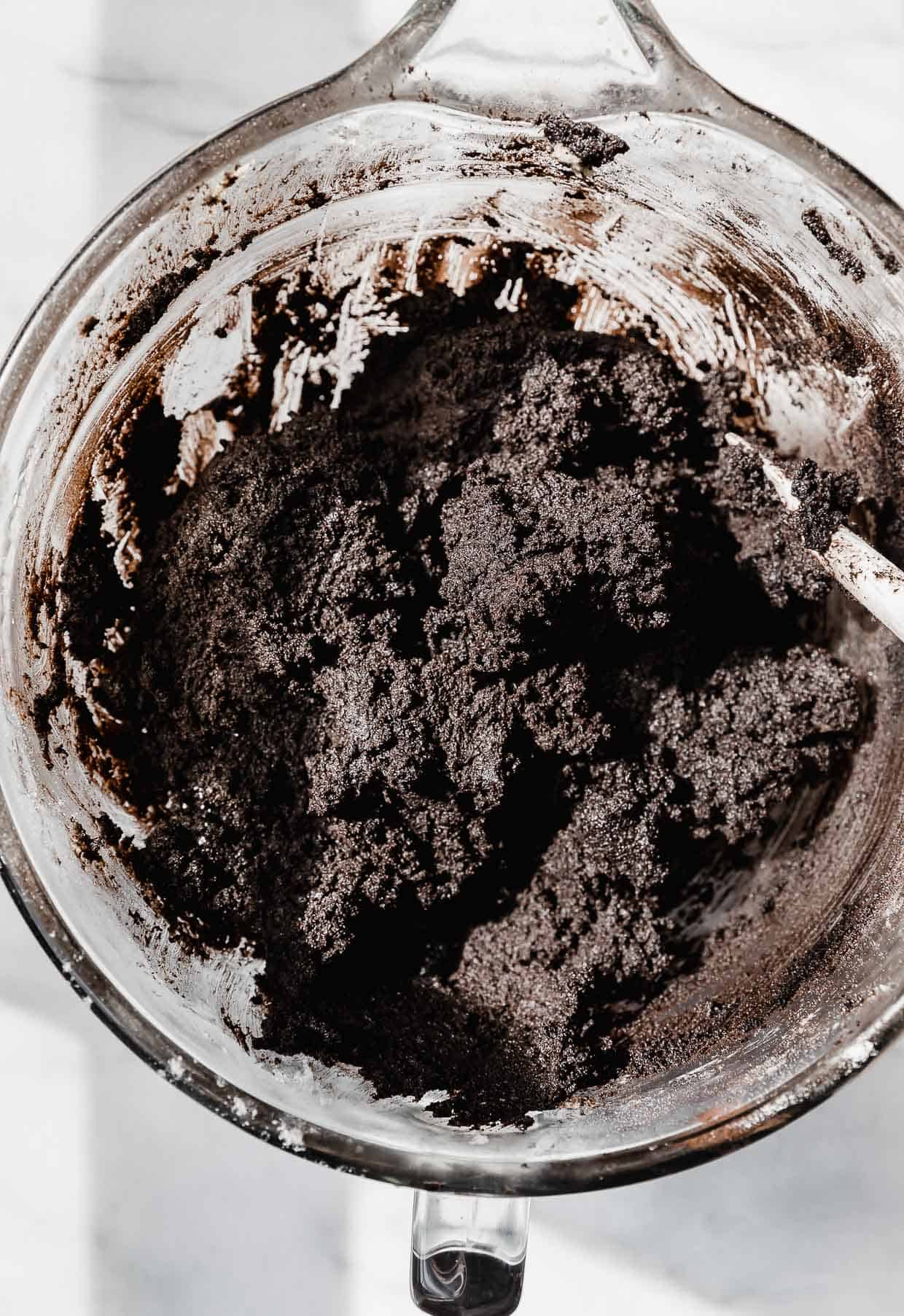Black oreo cookie dough in a glass mixing bowl.