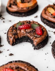 A Dirt Cake Cookie topped with Oreo crumbs and gummy worm with a bite taken out of the cookie.