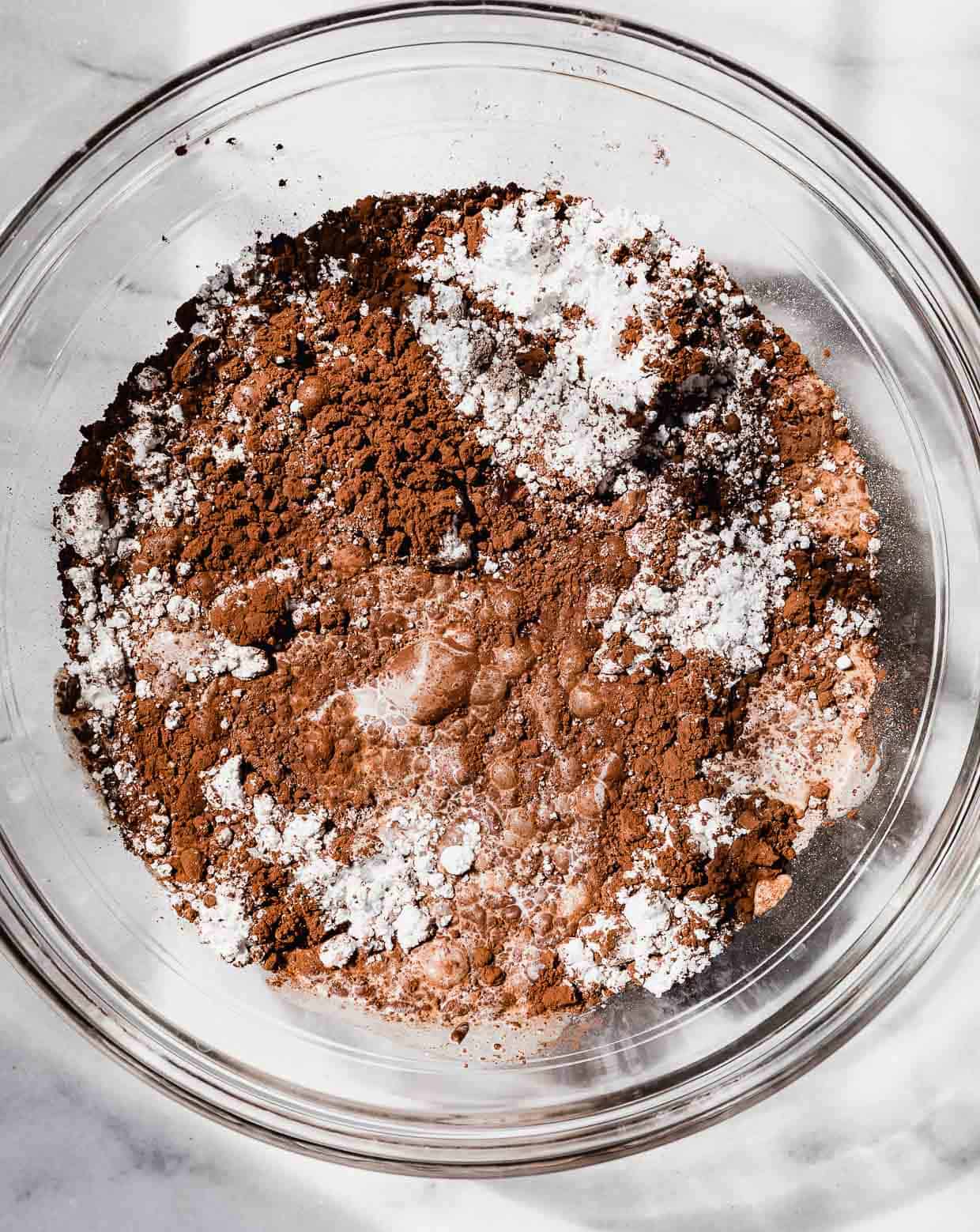 Cocoa powder, powdered sugar, and milk in a glass bowl on a marble background.