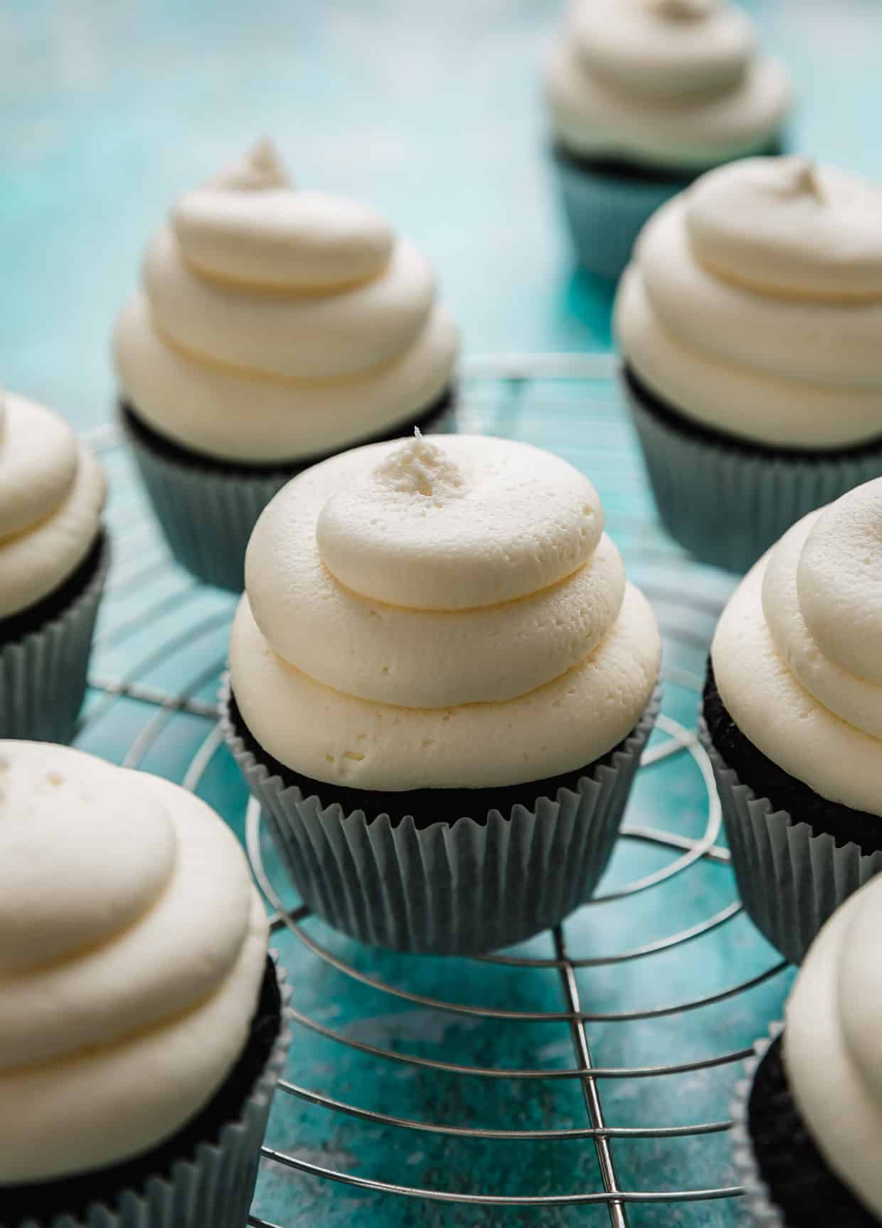 Chocolate cupcakes topped with a billowy smooth Whipped Cream Frosting on a turquoise background.