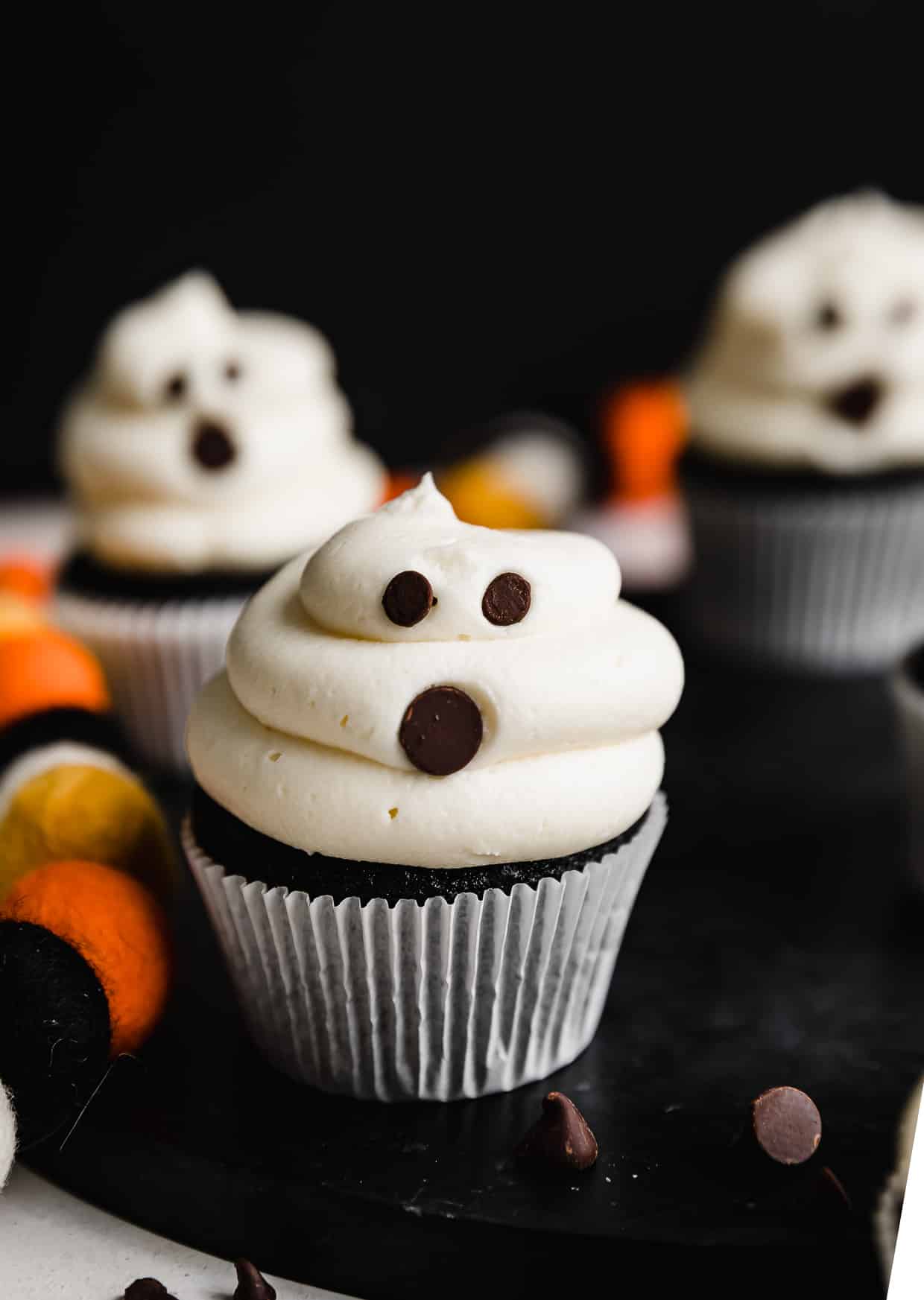 White frosting covered cupcakes with chocolate chips stuck into the frosting to make Ghost Cupcakes.