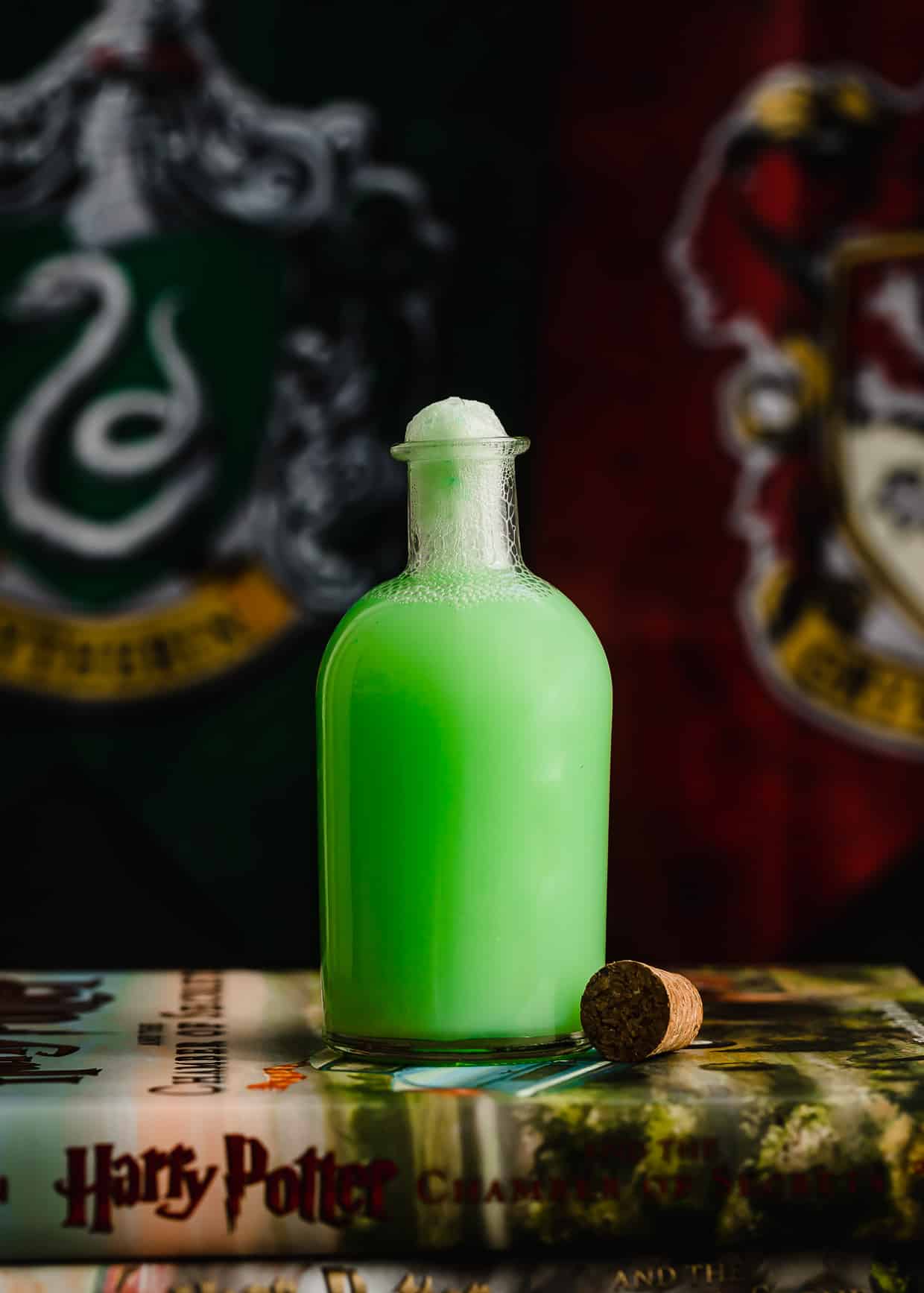 A potion jar filled with green Polyjuice Potion with a Slytherin and Gryffindor house flag in the background.