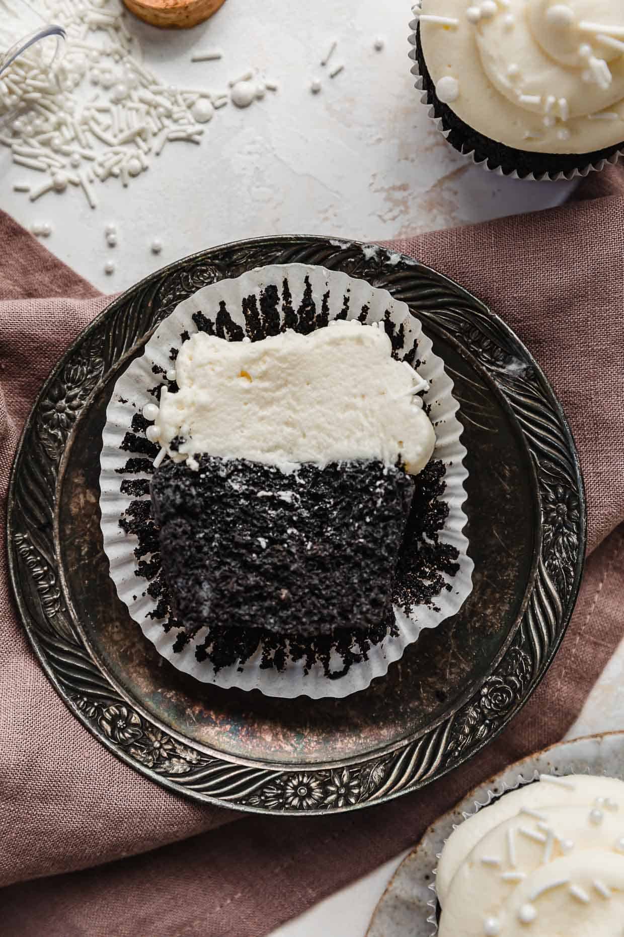 A black cocoa cupcake topped with homemade Whipped Cream Frosting cut in half, on a vintage plate.