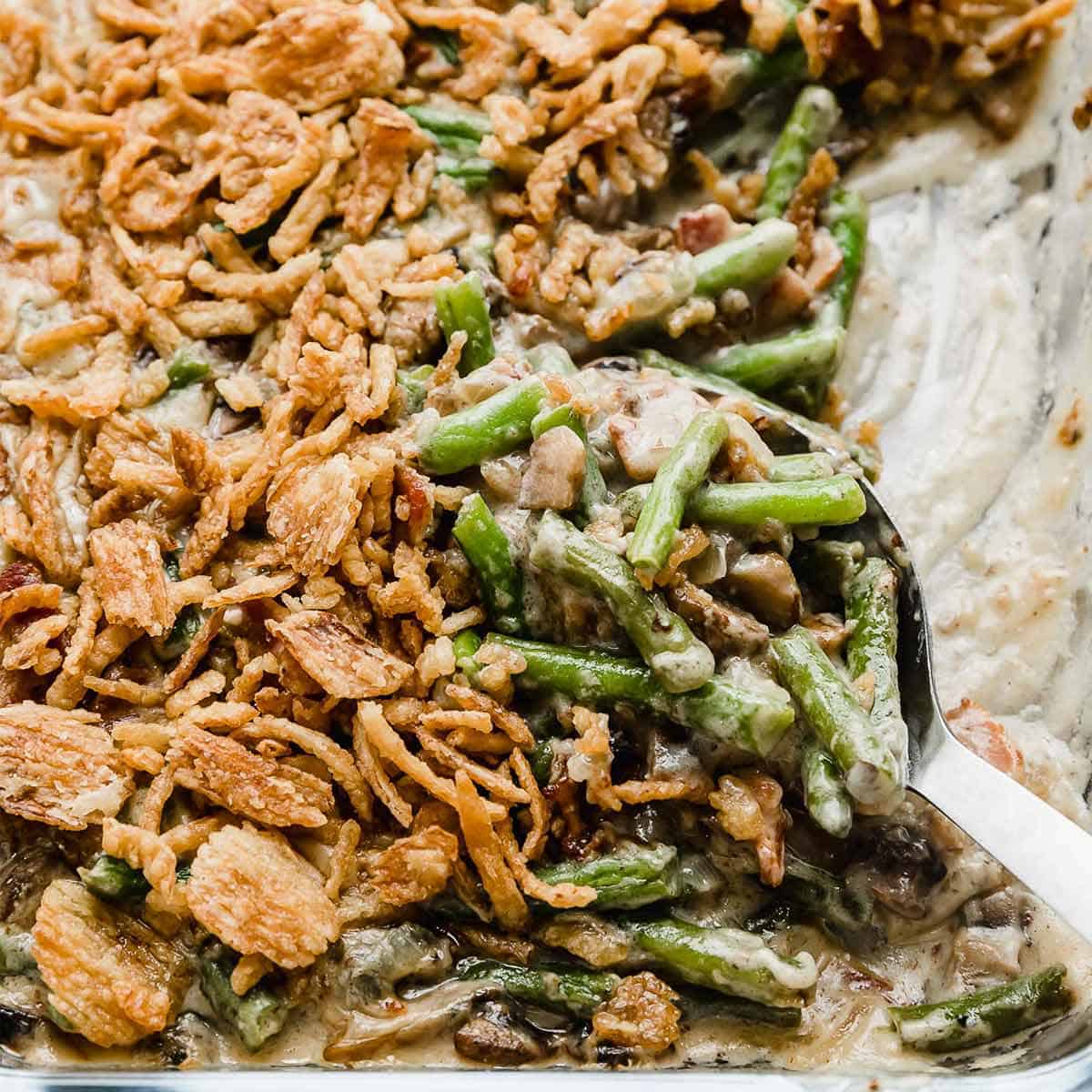 A serving spoon scooping out French fried onion topped Bacon Green Bean Casserole.