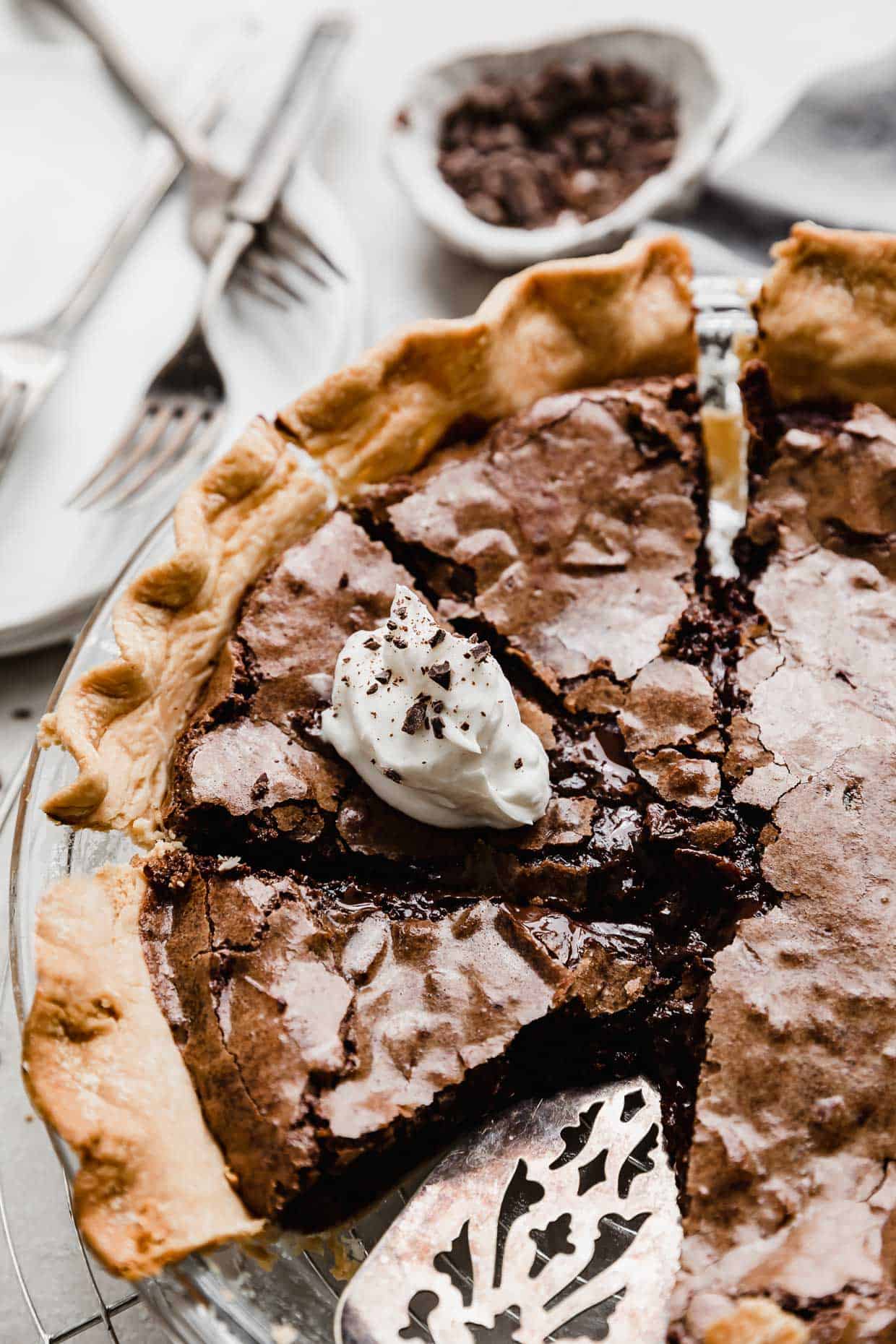 A Brownie Pie cut into slices, with one slice topped with white whipped cream and chocolate shavings.