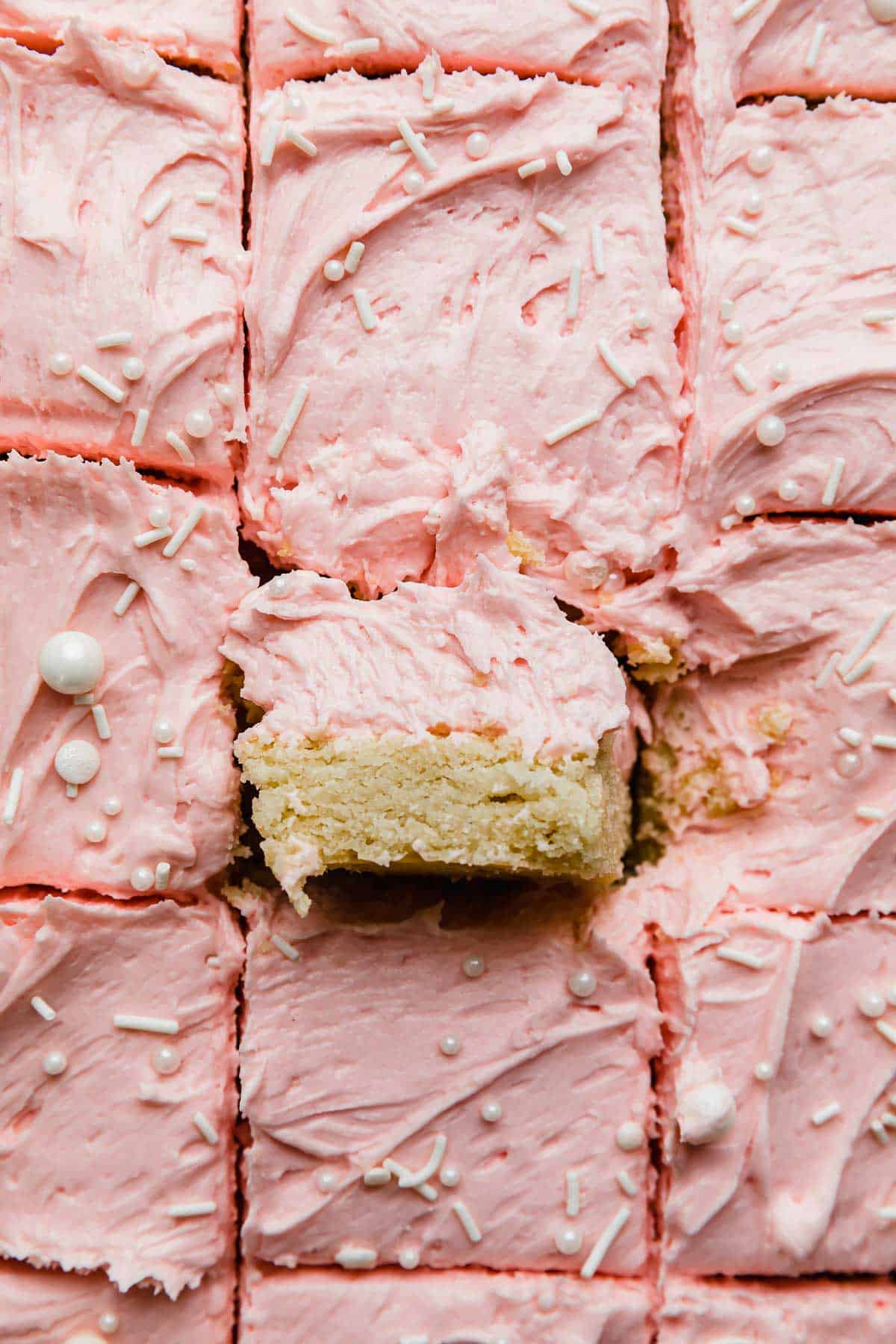 Sugar cookie bars cut into squares, topped with a swirl of pink frosting.