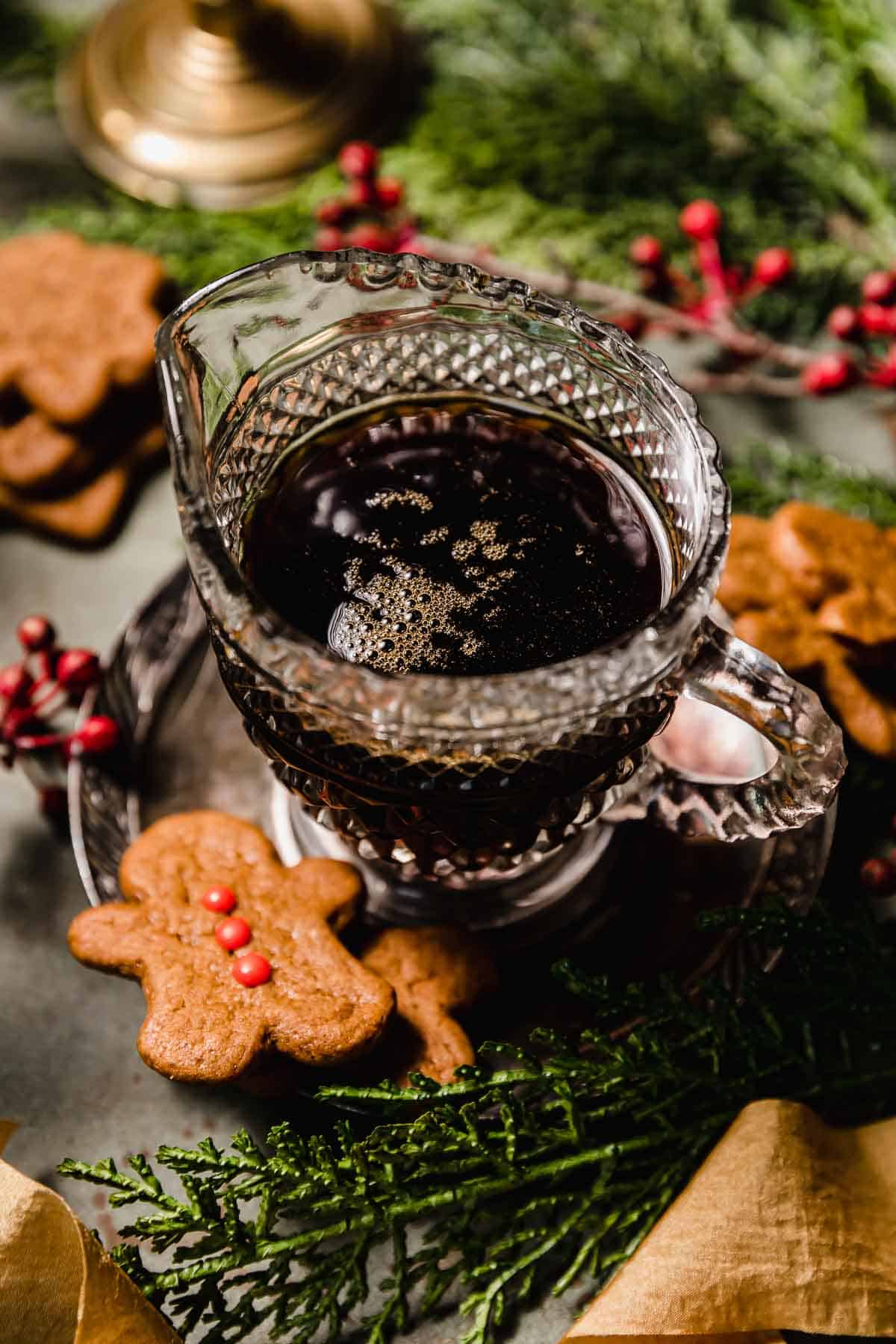 Gingerbread Syrup in a clear cup surrounded by baked gingerbread cookies, Christmas greenery, and red berries.
