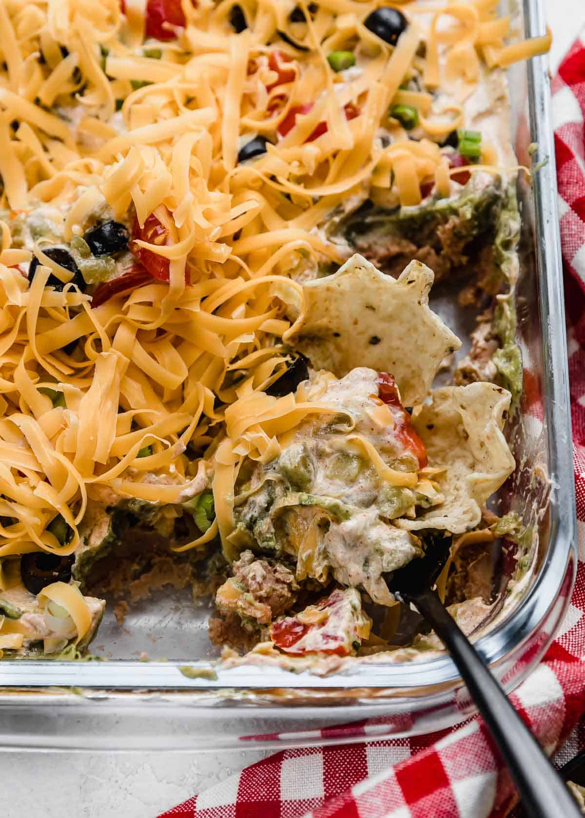A tortilla chip dipping into a Layered Taco Dip with refried beans, guacamole, sour cream, and cheese.
