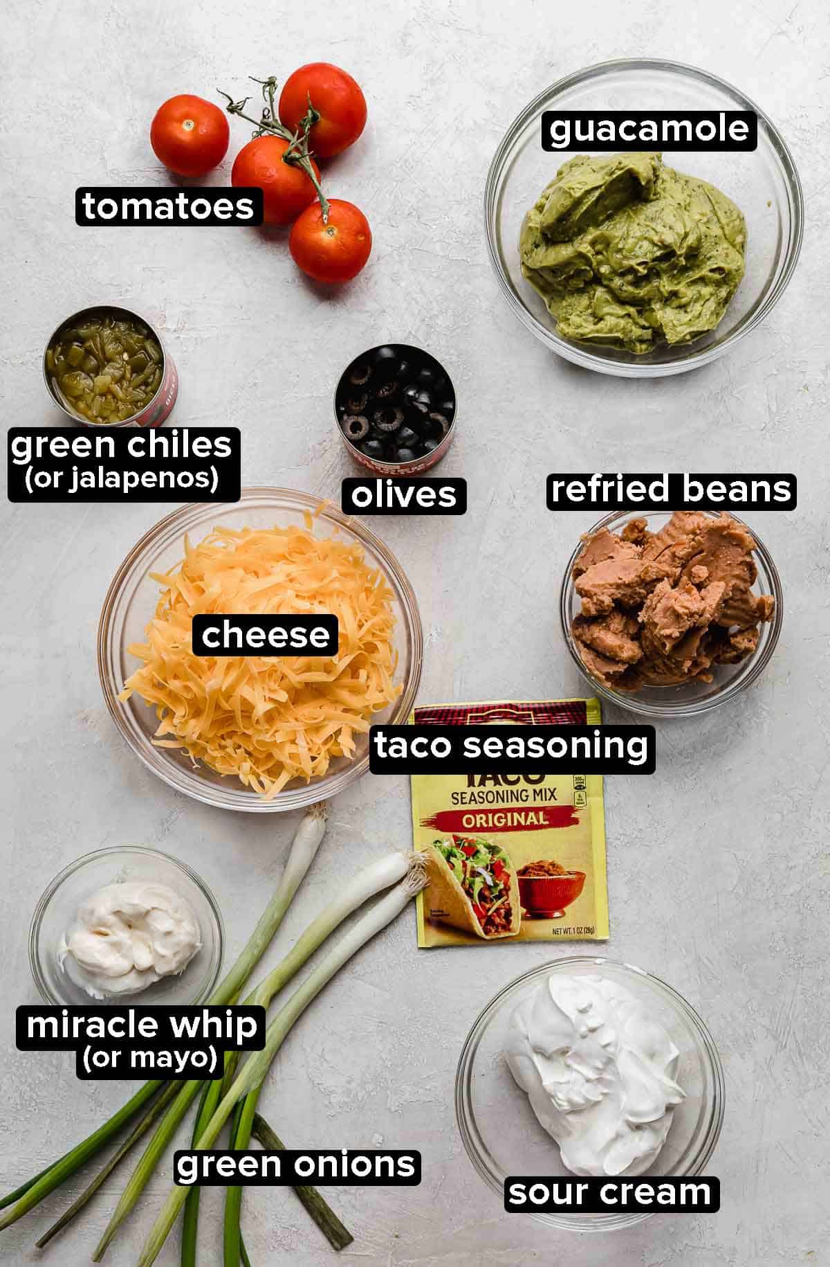 7 Layer taco dip ingredients portioned into glass bowls on a light gray background.