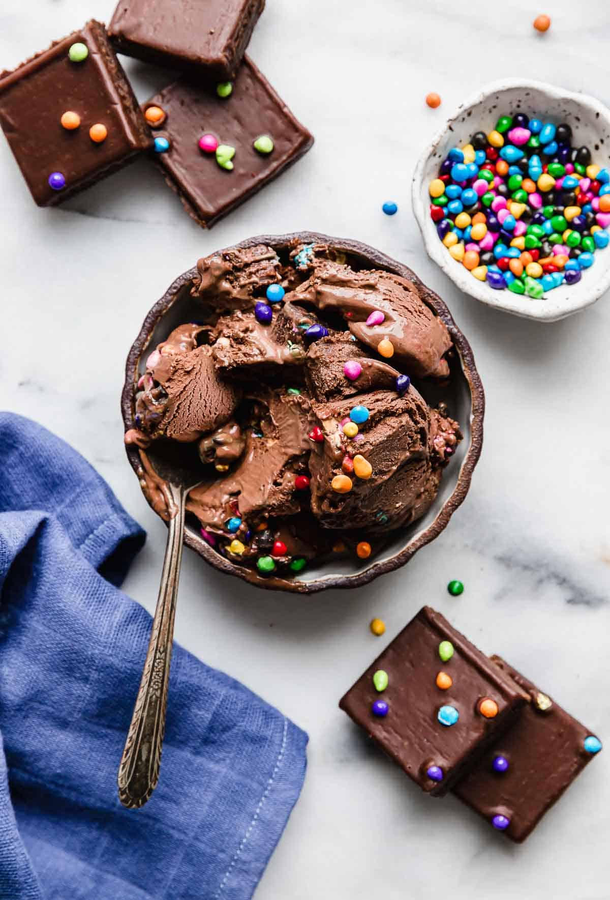 Overhead photo of Cosmic Brownie Ice Cream in a black rimmed bowl on a white background with a small bowl filled with cosmic colorful sprinkles.