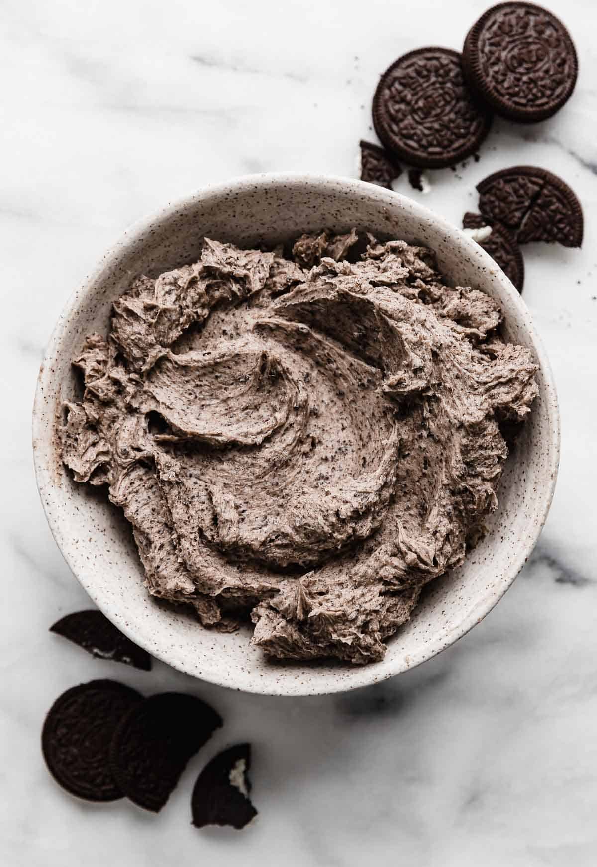 A white bowl filled with Oreo buttercream frosting (cookies and cream frosting) on a marble background.