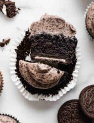 An Oreo Cupcake topped with Oreo frosting, that has been cut in half, exposing a full sized oreo on the bottom of the cupcake.