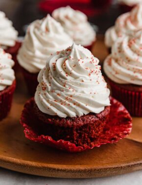 A Red Velvet Cupcake topped with cream cheese frosting, on a wooden plate.