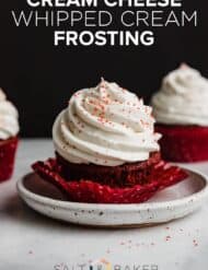 A red cupcake topped with swirled Cream Cheese Whipped Cream Frosting with the words, "Cream Cheese Whipped Cream Frosting" in white text over the photo.