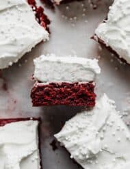 A Red Velvet Brownie square topped with a whipped cream frosting, laying on its side.