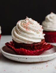 A red velvet cupcake topped with Cream Cheese Whipped Cream Frosting with red sugar sprinkles.
