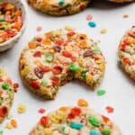 A Fruity Pebbles Cookie with a bite taken out of it, on a white background.