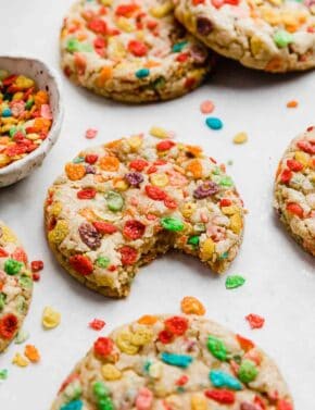 A Fruity Pebbles Cookie on a white background with a bite taken out of the cookie.