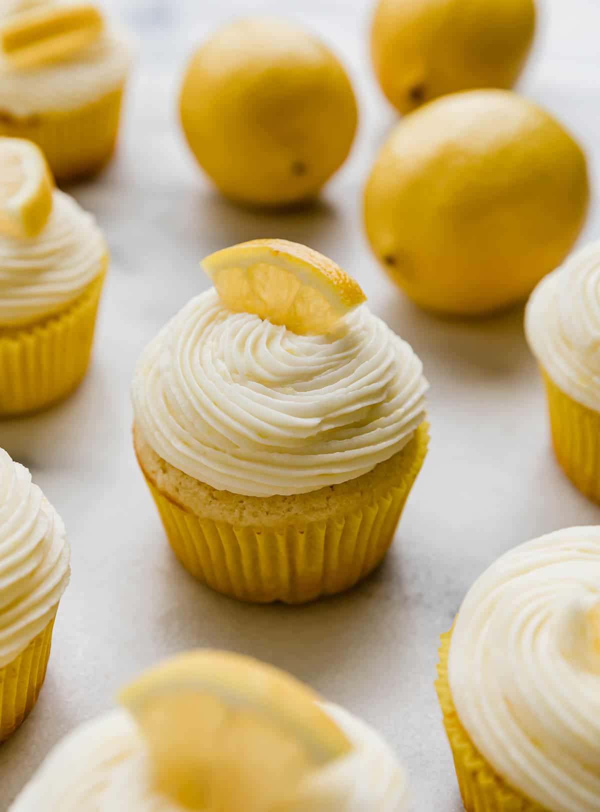 Lemon cupcakes topped with Lemon Buttercream and a fresh lemon wedge on a white background.