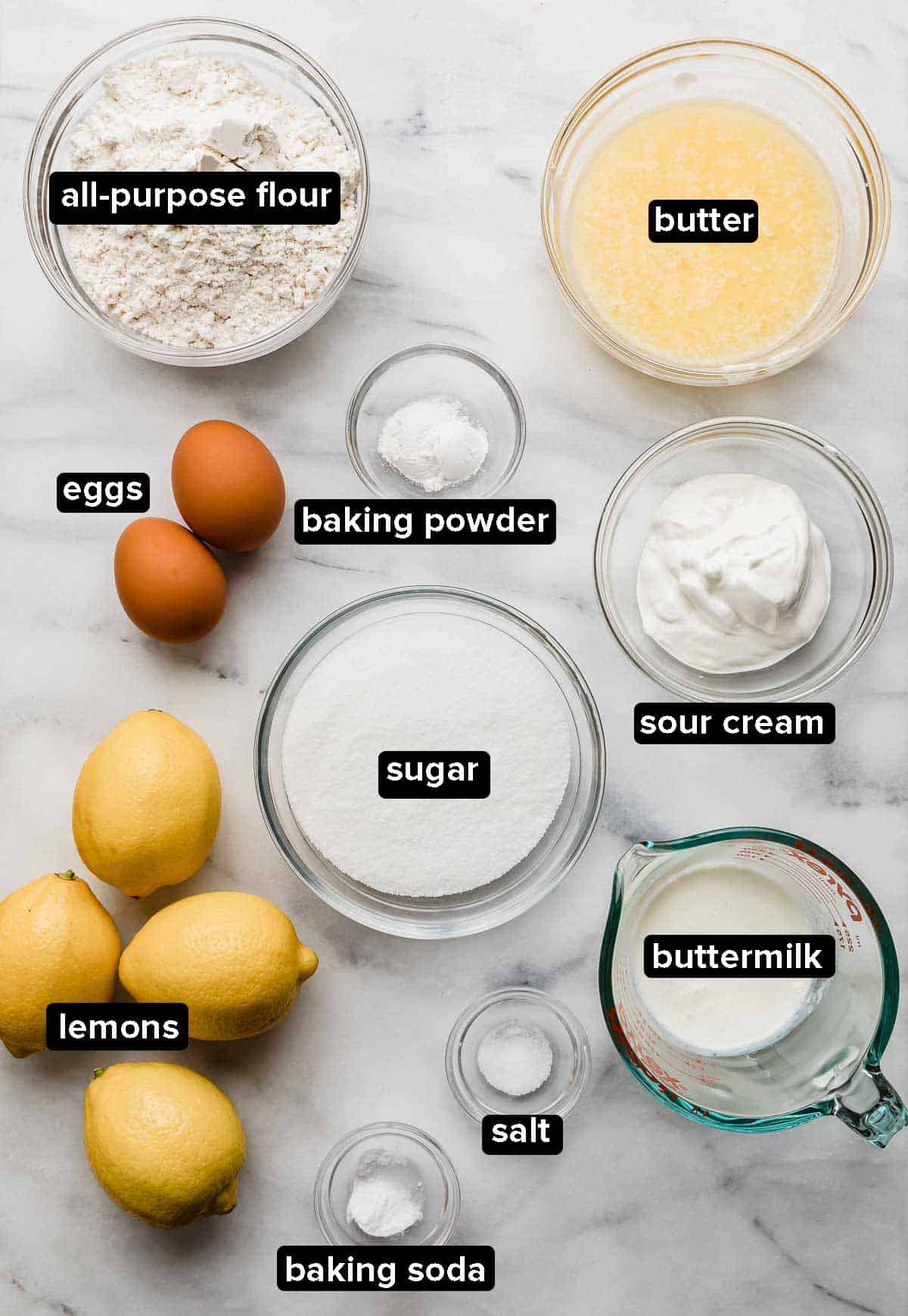 Lemon Cupcake ingredients portioned into glass bowls on a white marble background.