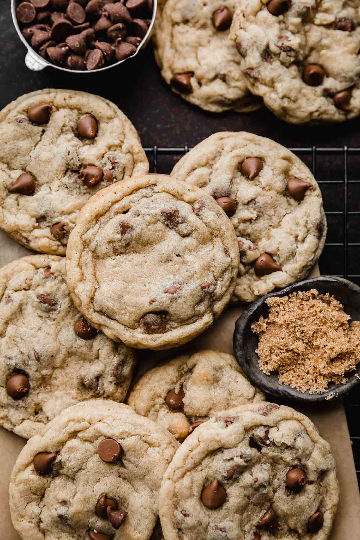 Milk Chocolate Chip Cookies on a black cooling rack with a small bowl of brown sugar and milk chocolate chips near the cookies.