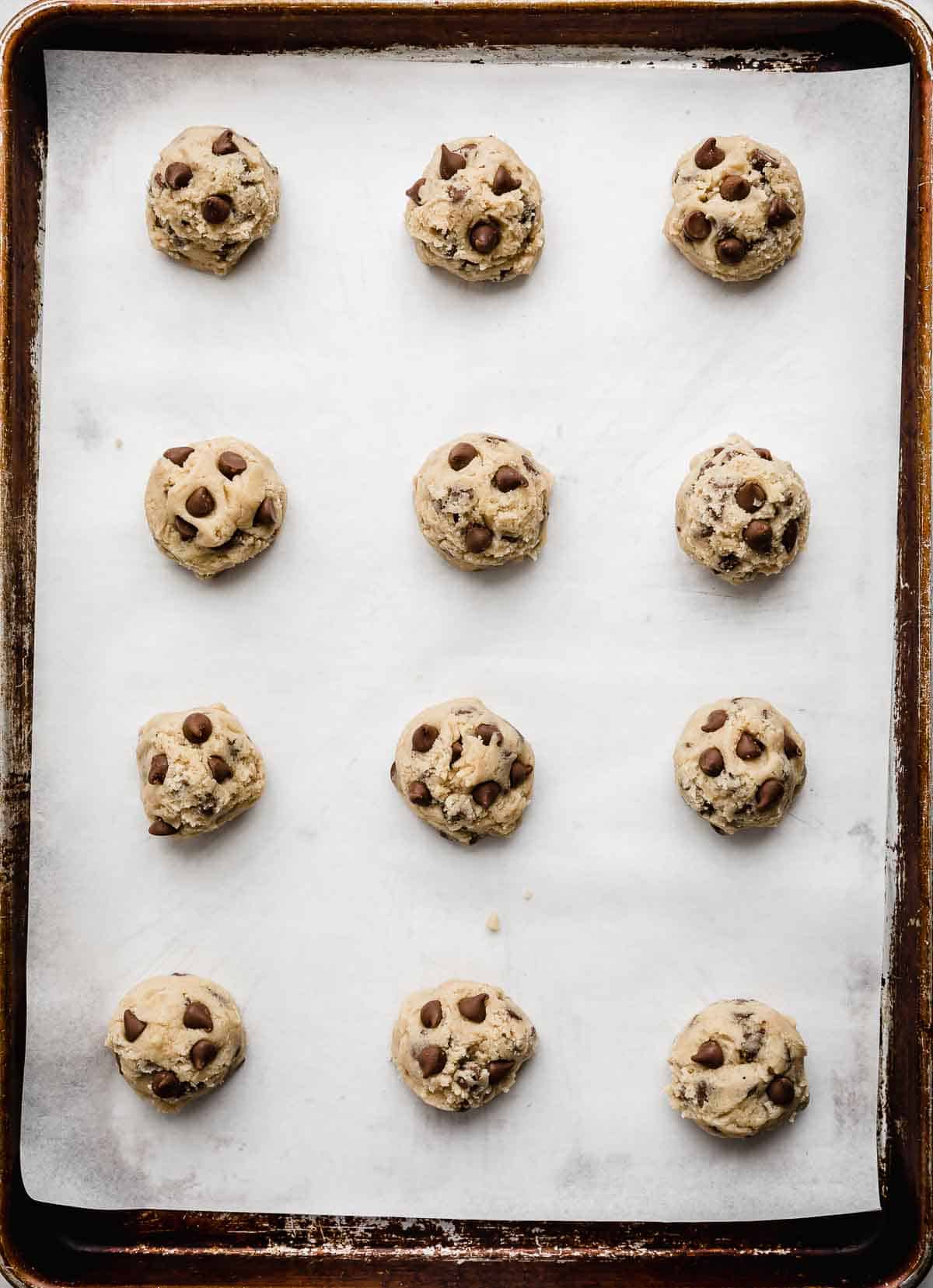 Milk Chocolate Chip Cookie dough balls on a white parchment lined baking sheet.